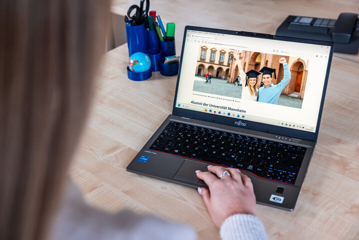 An einem Laptop ist die Alumni-Webseite der Universität geöffnet. Eine Hand liegt auf dem Touchpad.