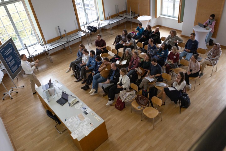 Seminarraum von oben fotografiert. Prof. Dr. Markus Strohmaier hält einen Vortrag vor etwa 30 Zuhörenden.