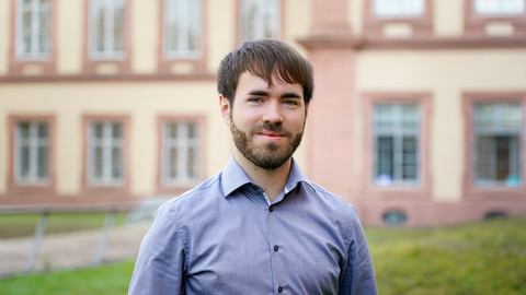 Michael Imre. He is wearing a blue shirt and is standing on the Mensawiese in front of the castle.