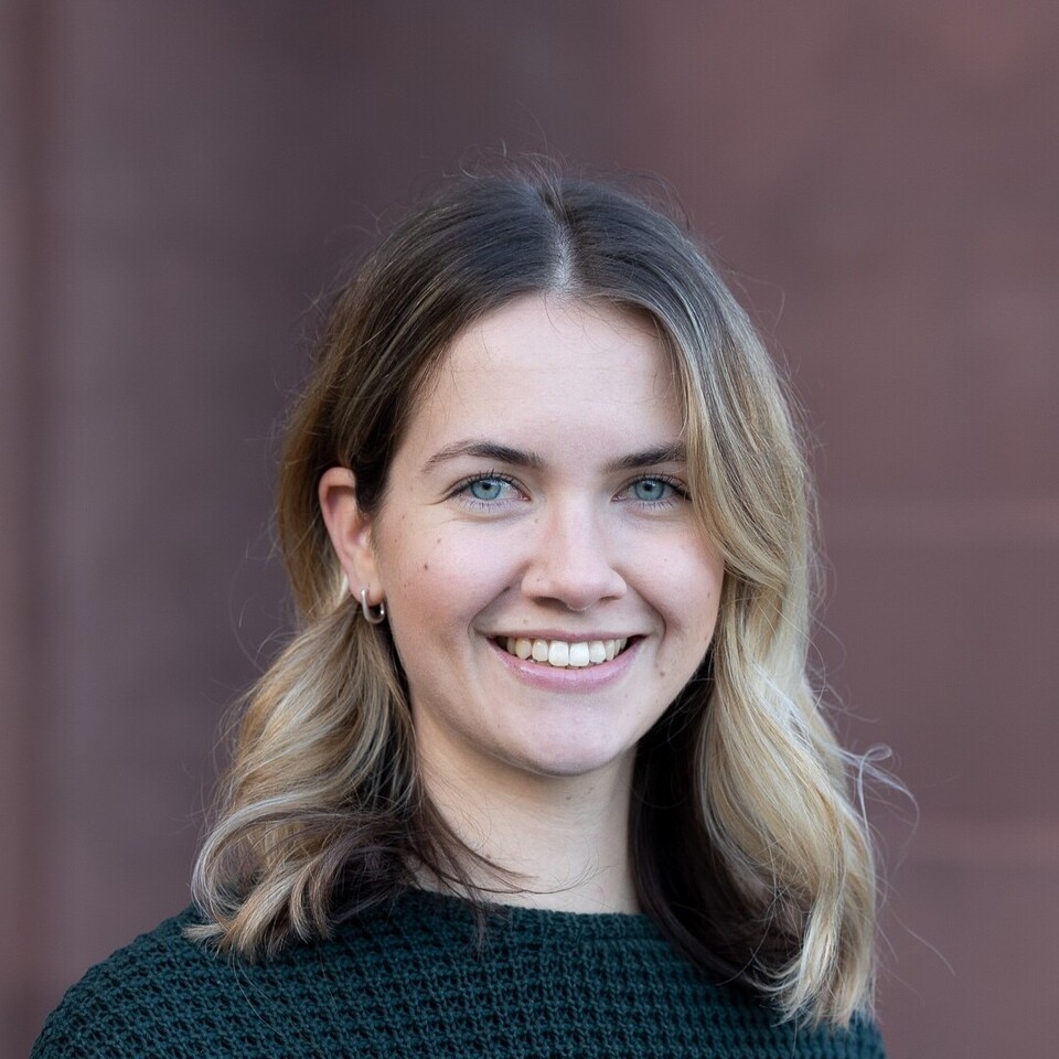  Klara Müller steht vor dem Mannheimer Schloss. Sie hat schulterlanges blondes Haar und trägt einen schwarzen Pullover.