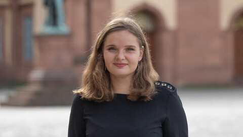 Daria Frost. She is wearing a black sweater and is standing on the Ehrenhof in front of the castle.