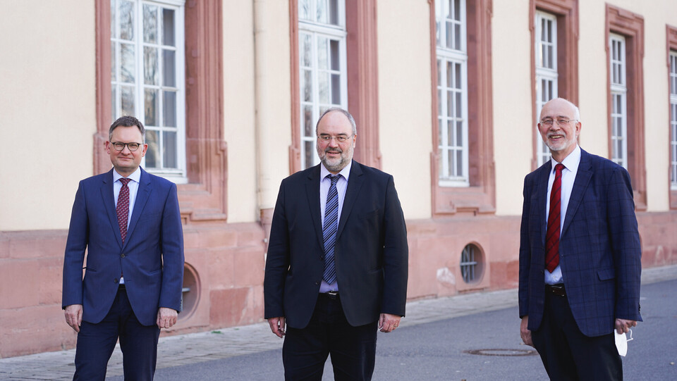 Drei Personen in anzug und Krawatte stehen vor dem Mannheimer Schloss. 