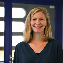 Cosima Meyer hat mittellange blonde Haare. Sie trägt ein buntes Oberteil und lächelt in die kamera.