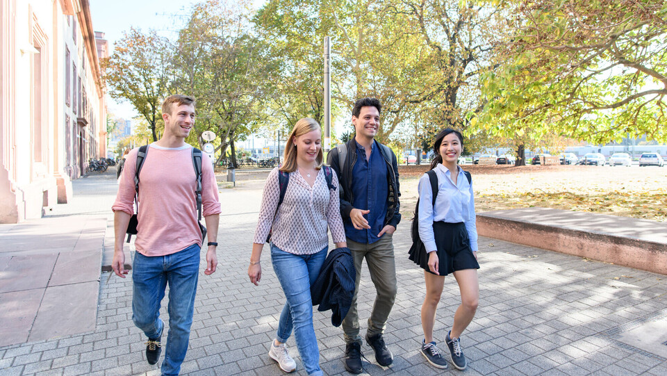 Students of the program in Business Informatics and Mathematics Four students are walking on a path in front of the castle, laughing
