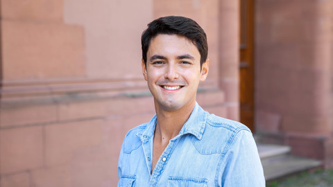 João Areal Neto. He is wearing a blue shirt and is standing in front of a brown stonewall.