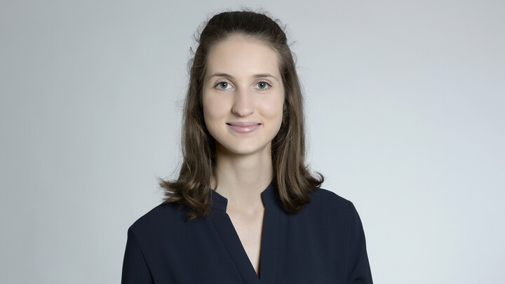 Julia Spix. She is wearing a black shirt and is standing in front of a grey wall.