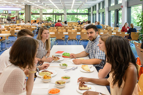 Studierende sitzen gemeinsam in der Mensa an einem Tisch und essen zu Mittag.