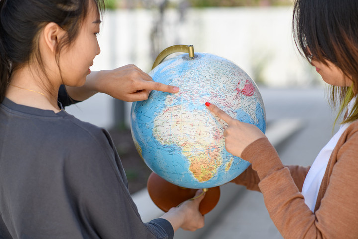 Zwei internationale Forscherinnen halten einen Standglobus in der Hand, während die eine auf Belgien zeigt und die andere auf die Türkei.