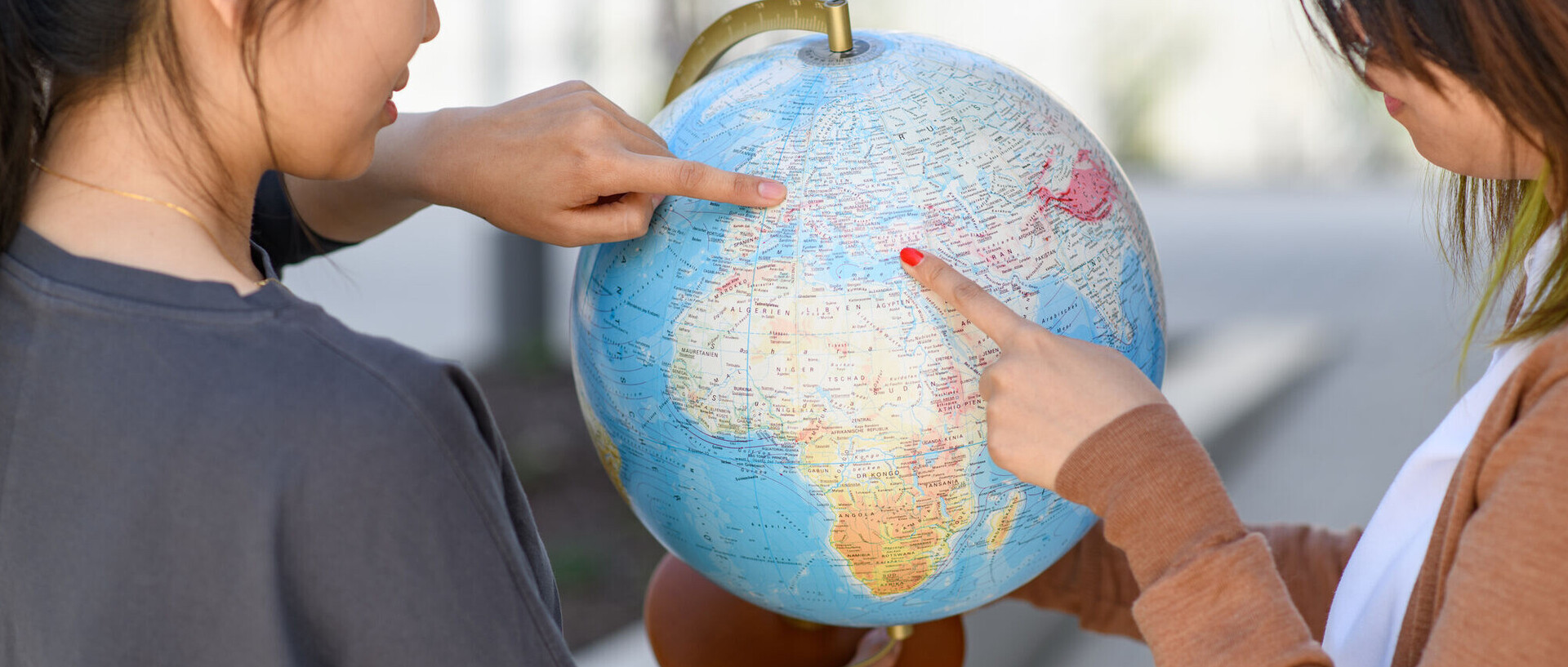 Zwei internationale Forscherinnen halten einen Standglobus in der Hand, während die eine auf Belgien zeigt und die andere auf die Türkei.