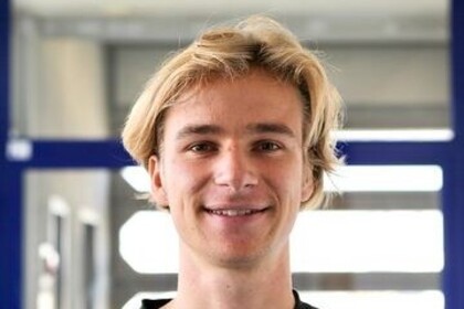 Oliver Rittmann steht vor einer Glastür. Er trägt einen dunklen Pullover und hat hellblonde Haare.
