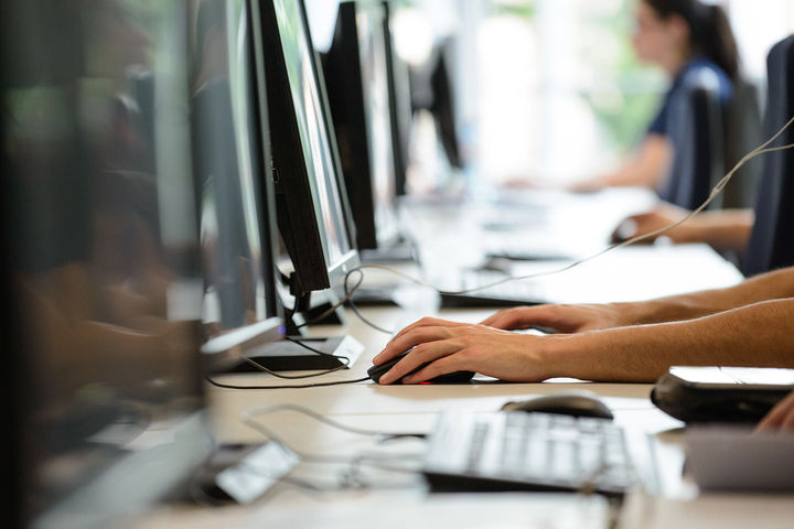 Vier Menschen sitzen in einer Reihe vor Computern.