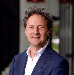 Guido van Leerzem hat graue, lockige Haare. Er trägt ein blaues Jacket und eine weiße Bluse.
