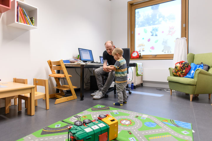 Vater und Sohn sitzen in einem Spielraum, der Vater zeigt dem Sohn etwas.