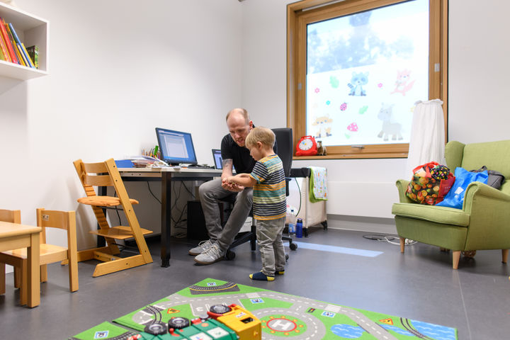 Vater und Sohn sitzen in einem Spielraum, der Vater zeigt dem Sohn etwas.