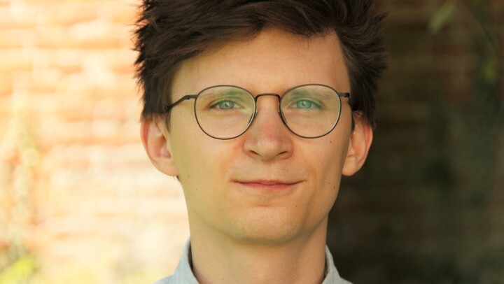 Marius Cziriak. He is wearing a blue shirt and is standing outside in front of brick wall.