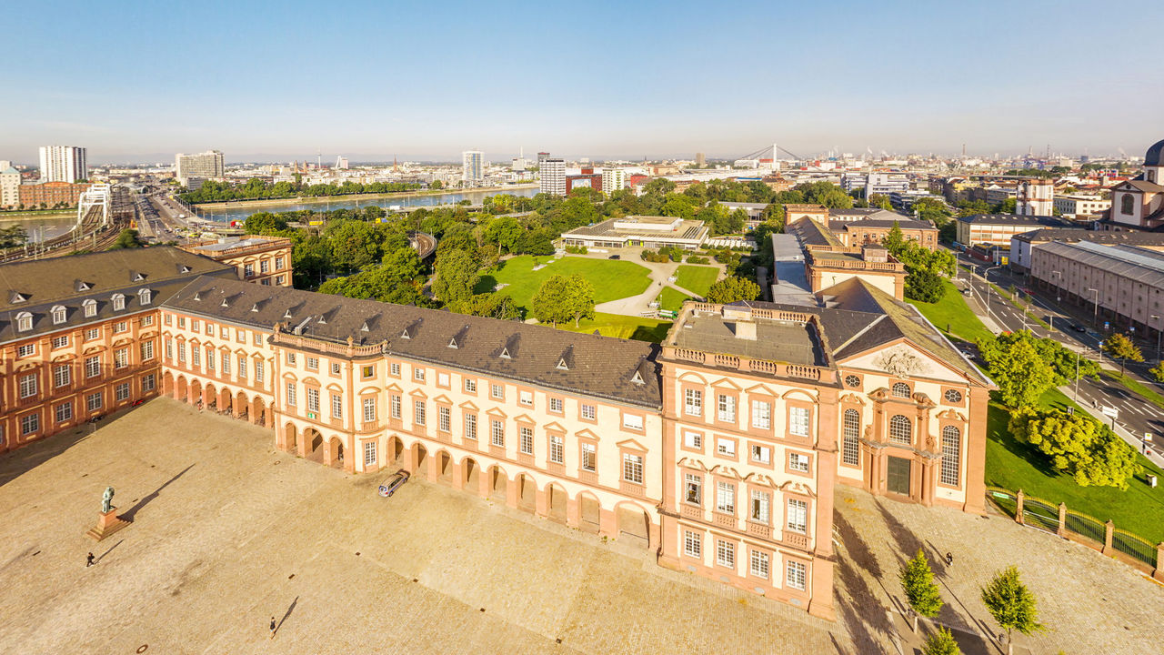 Vogelperspektive auf den Ehrenhof und das Mannheimer Schloss. Dahinter die grüne Mensawiese, die Konrad-Adenauer-Brücke und der Rhein.