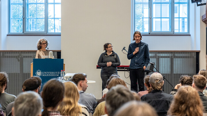 Dr. Rittmann und Prof. Steinbeger stehen auf der Bühne und Dr. Rittmann hält ein Mikrofon in der Hand. Er beantwortet Fragen aus dem Publikum.