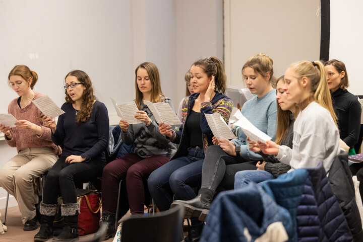 Mitgliederinnen des Unichors sitzen beisammen und singen.