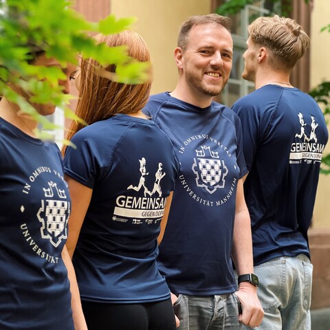 Vier Studierende stehen in einer Reihe, abwechselnd mit dem Gesicht zur Fotografin beziehungsweise abgewendet. Sie tragen das blaue Lauf-Shirt der Universität Mannheim.