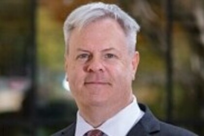 Alvin Malesky hat kurze graue Haare. Er trägt ein weißes Hemd, eine rote Krawatte und ein schwarzes Jackett.