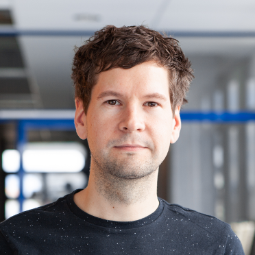 Christoph Kern in einem Flur mit Glastüren im Hintergrund. er trägt ein dunkles Shirt.