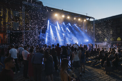 Die Bühne auf dem Ehrenhof vor dem Schloss Mittelbau ist in blaues Licht getaucht. Drei Musiker der Band Kabinett stehen auf der Bühne, im Vordergrund ist ein Teil des Publikums zu sehen.