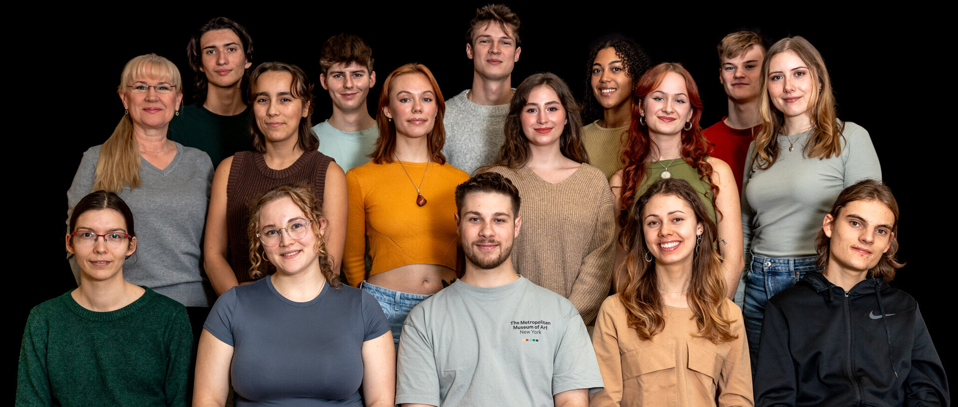 Eine Gruppe von 16 Personen sitzt beziehungsweise steht in drei Reihen hintereinander.