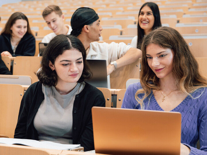 Junge Menschen sitzen im Vorlesungssaal. Einige haben Laptops vor sich.