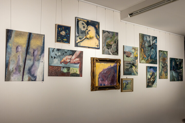 An einer weißen Wand sind abstrakte Gemälde ausgestellt, hauptsächlich in blauen Farbtönen. 