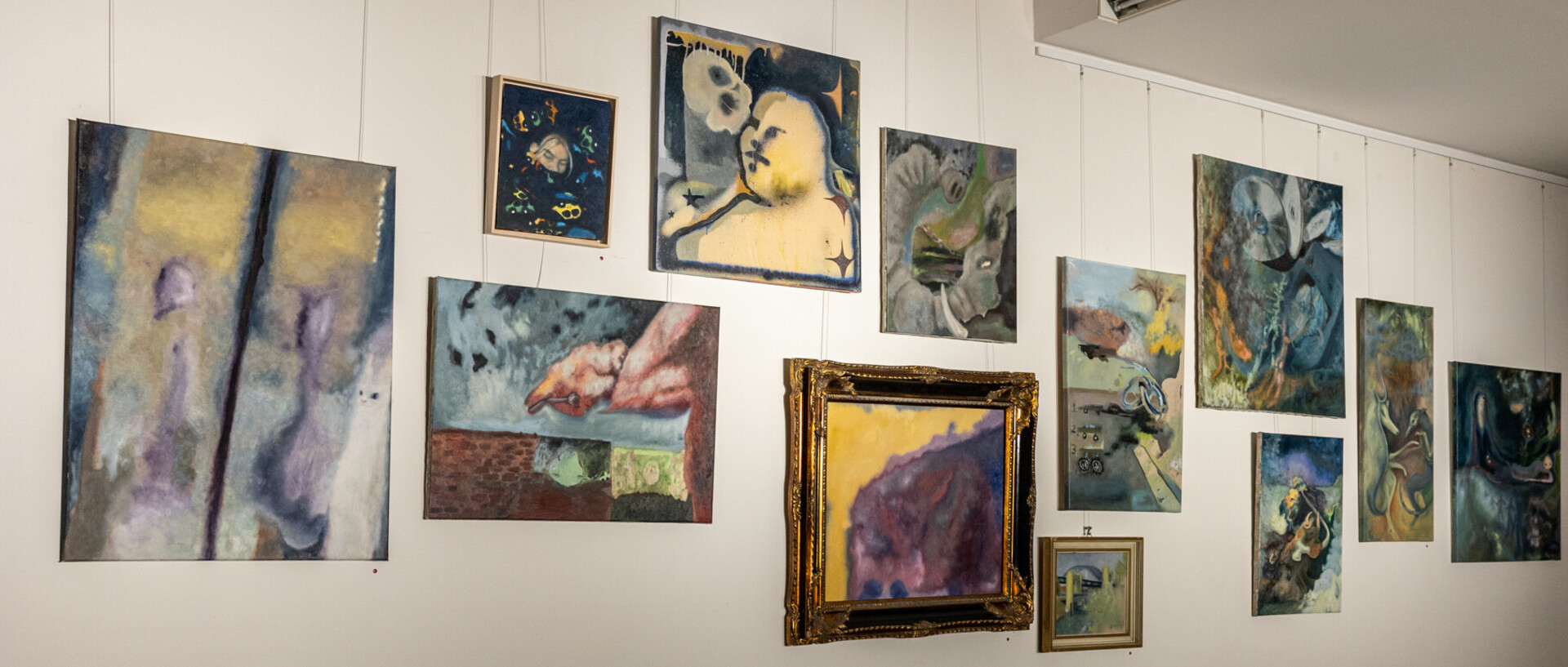 An einer weißen Wand sind abstrakte Gemälde ausgestellt, hauptsächlich in blauen Farbtönen.