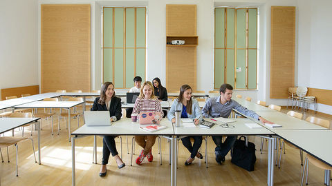 Sechs Studierende arbeiten in einem Seminarraum. Vor ihnen liegen Laptops, Notizblöcke und Bücher.