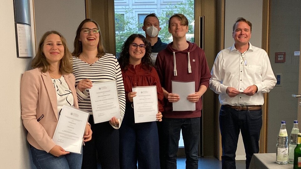 A group photo showing, from left to right, Fabienne Partsch, Hannah Rajski, Malena Ullrich, Leonard Wendering, Julius Diener, and Harmut Höhle, all smiling. The award winners are holding their award certificates toward the camera.