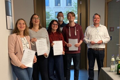 A group photo showing, from left to right, Fabienne Partsch, Hannah Rajski, Malena Ullrich, Leonard Wendering, Julius Diener, and Harmut Höhle, all smiling. The award winners are holding their award certificates toward the camera.