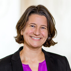 Dr. Katrin Schoppa-Bauer hat braune mittellange Haare. Sie trägt einen schwarzen Blazer und eine lilafarbene Bluse.