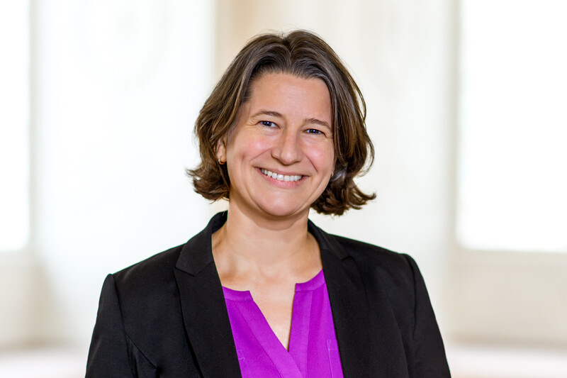 Dr. Katrin Schoppa-Bauer hat braune mittellange Haare. Sie trägt einen schwarzen Blazer und eine lilafarbene Bluse.