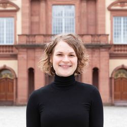 Marie-Aimee Salopiata hat blondes, kinnlanges, lockiges Haar und lächelt. Sie trägt einen schwarzen Rollkragenpullover.