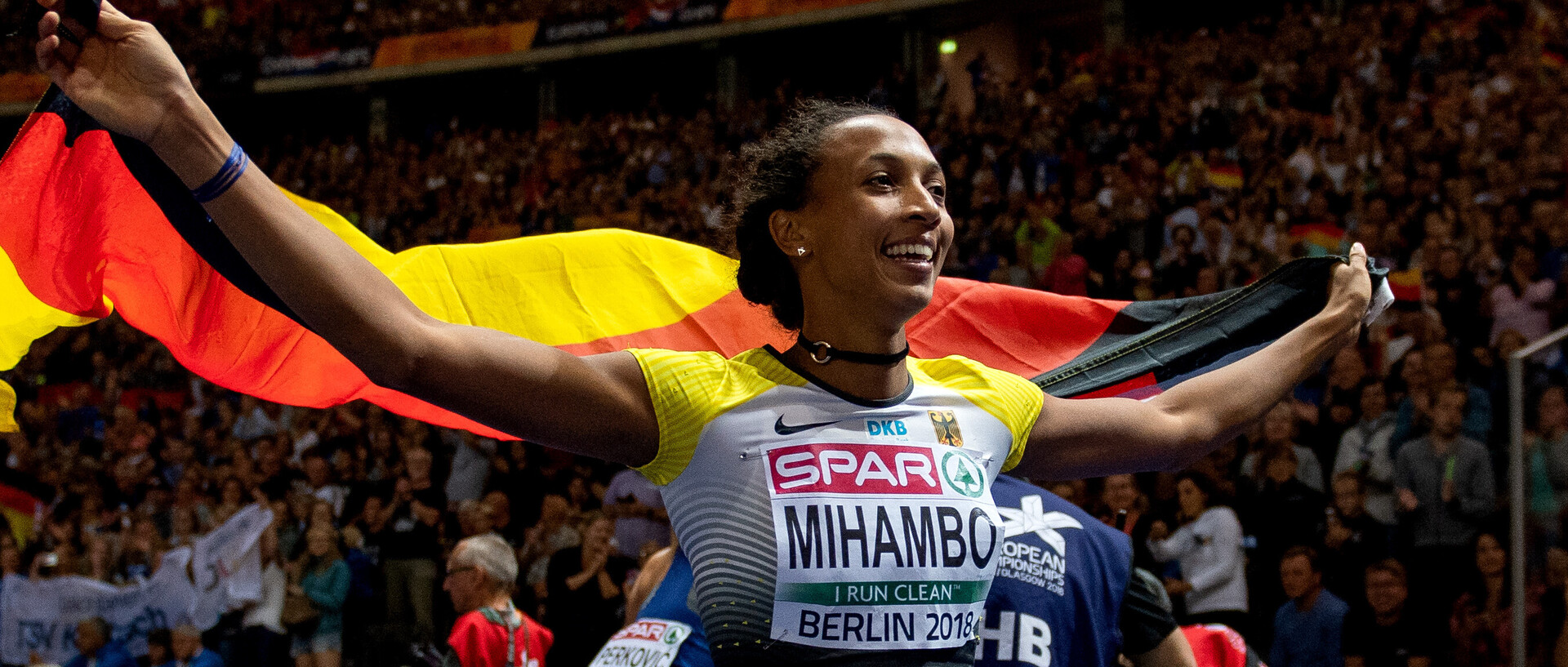 Malaika Mihambo bei der EM: Sie trägt Sportkleidung und hält eine Deutschland-Flagge.