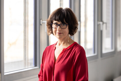 Prof. Kogan trägt ein rotes Oberteil und eine Brille.