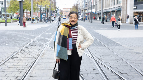 Eine Studentin mit heller Wolljacke und buntem Schal steht auf den Bahngleisen in den Quadraten