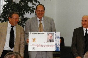 Pärsentation des Studierendenausweises im Jahr 2000. Eine männlich gelesene Person hält ein riesiges Exemplar eines Ausweises in den Händen.