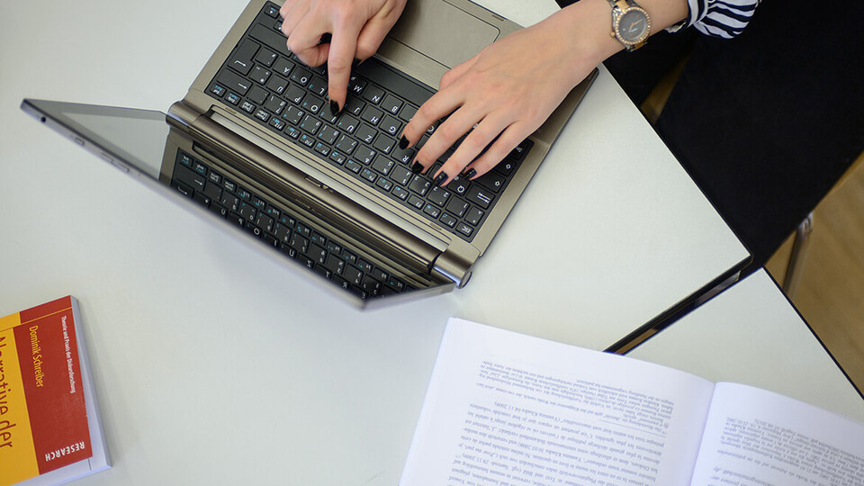 Zwei Hände einer Frau tippen auf der Tastatur eines Laptops.