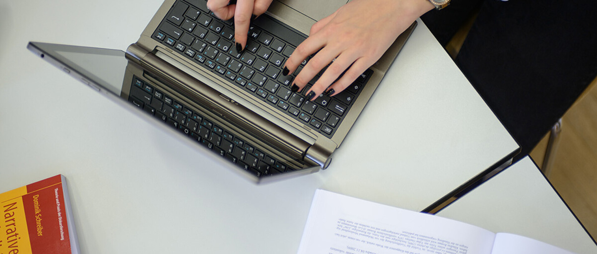 Zwei Hände einer Frau tippen auf der Tastatur eines Laptops.