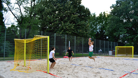 Drei Personen in Sportkleidung spielen Beachhandball im Freien.