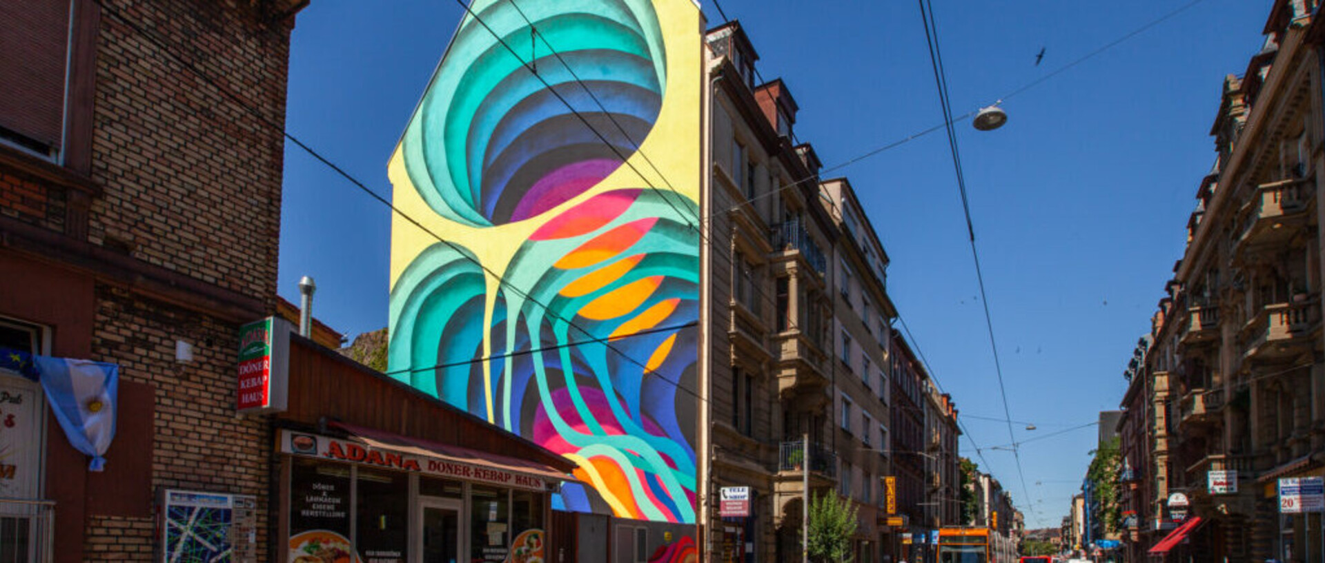 Eine Hauswand ist bunt bemalt. Daneben velaufen Straßenbahnschienen.