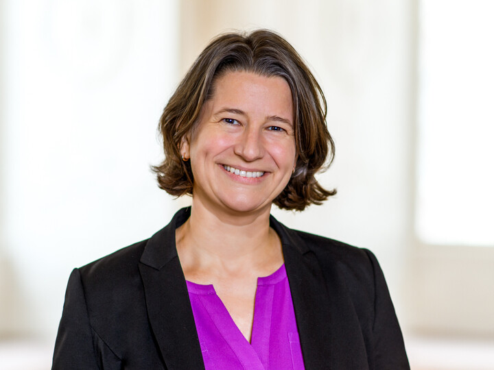 Dr. Katrin Schoppa-Bauer hat braune mittellange Haare. Sie trägt einen schwarzen Blazer und eine lilafarbene Bluse.