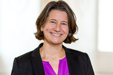 Dr. Katrin Schoppa-Bauer hat braune mittellange Haare. Sie trägt einen schwarzen Blazer und eine lilafarbene Bluse.