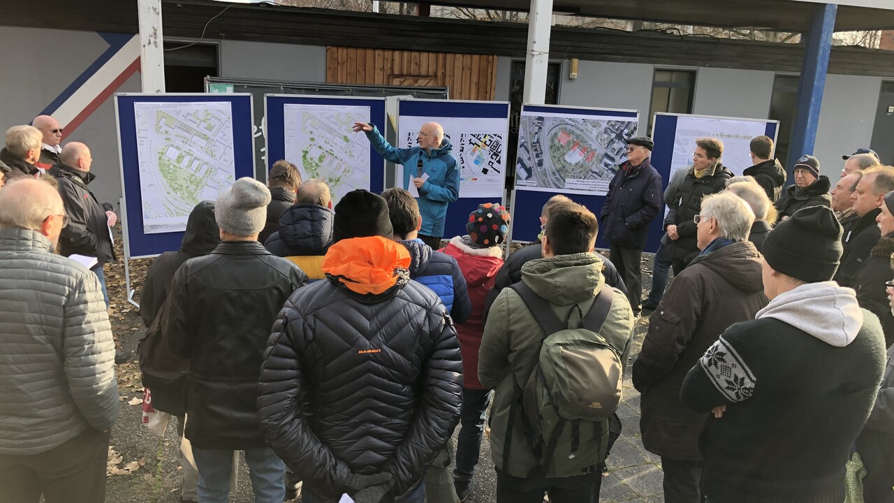 Rektor Prof. Dr. Thomas Puhl präsentiert die Pläne zur Bebauung des Friedrichparks. Er zeigt auf Plakate des Rahmenplans und Skizzen. Um ihn herum sind Zuschauende.
