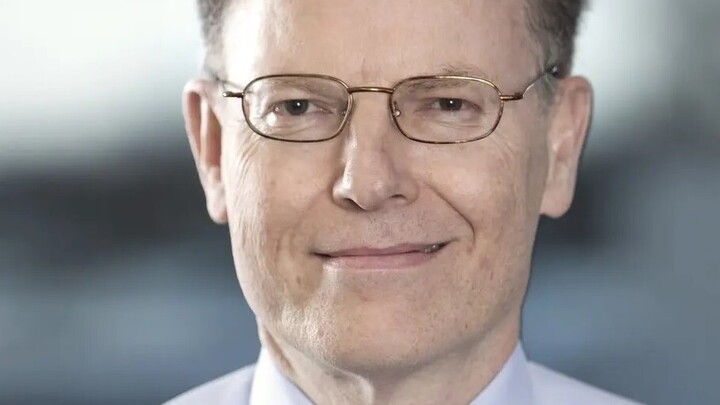 Professor Dr. Colin Atkinson trägt ein helles Hemd, Krawatte und eine Brille und lächelt in die Kamera.