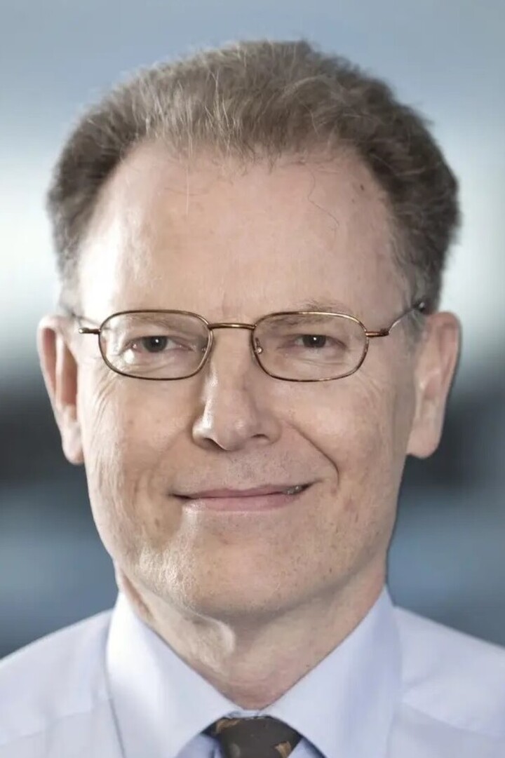 Professor Dr. Colin Atkinson trägt ein helles Hemd, Krawatte und eine Brille und lächelt in die Kamera.