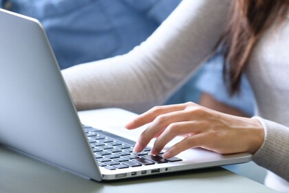 Eine Studentin schreibt an einem Laptop, im Bild sind die Arme, die linke Hand am Laptop, der Oberkörper und lange braune Haare. Das Laptop steht auf einem Tisch im ExpLAB im Bibliotheksbereich Schloss Schneckenhof.